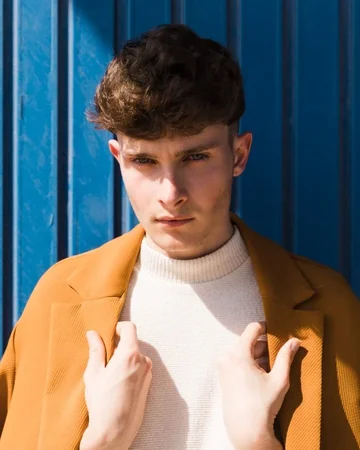 Man in a mustard jacket against a blue wall