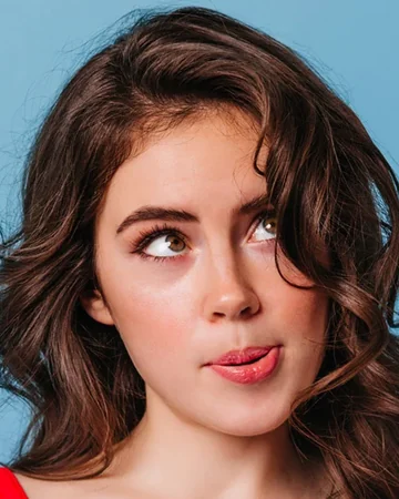 Woman with curly hair blowing a curl off her face against a blue wall
