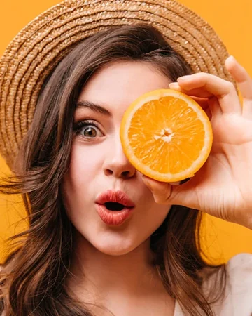Woman in a straw hat holding an orange slice over one eye